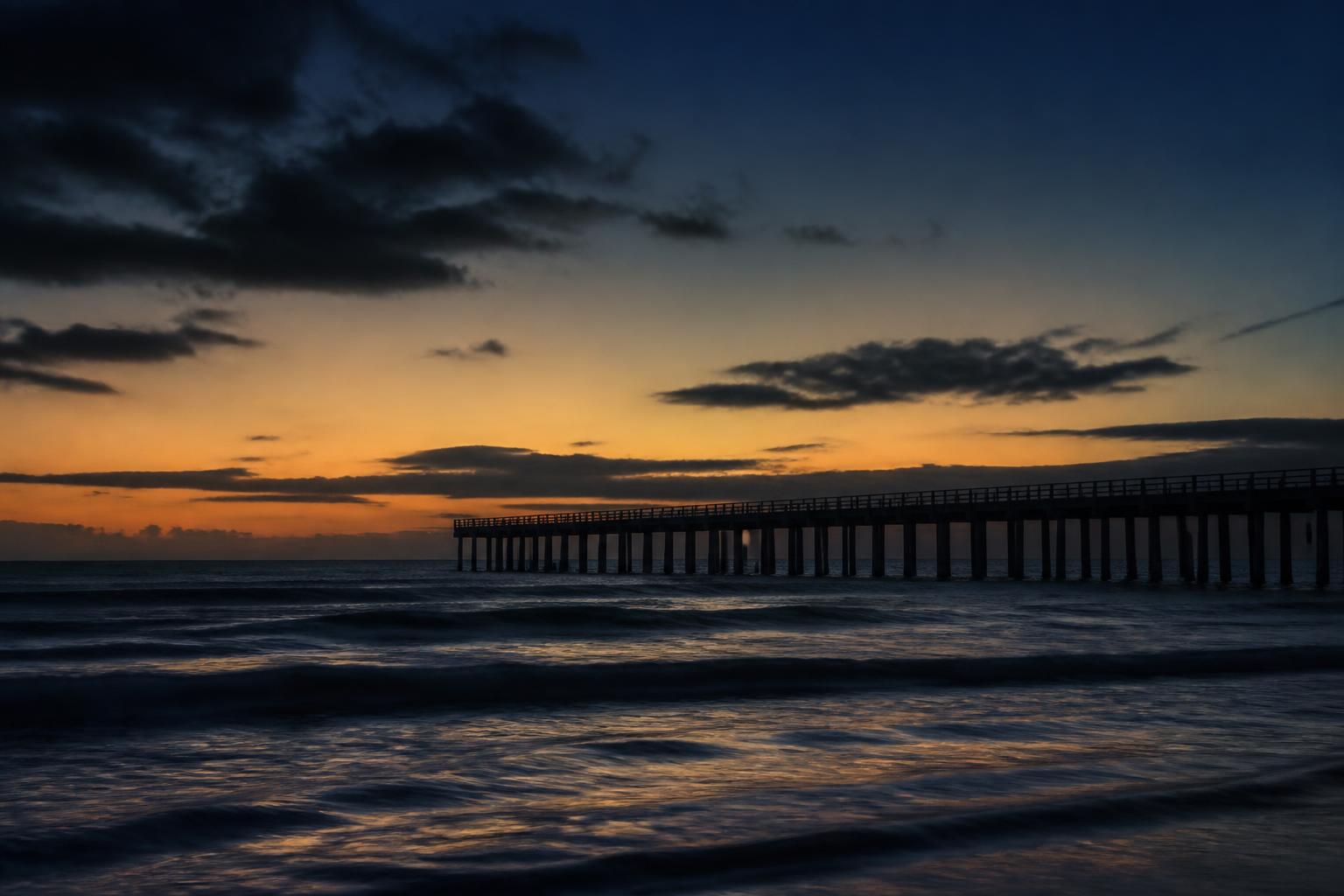 Distant pier silhouette over dark ocean water
